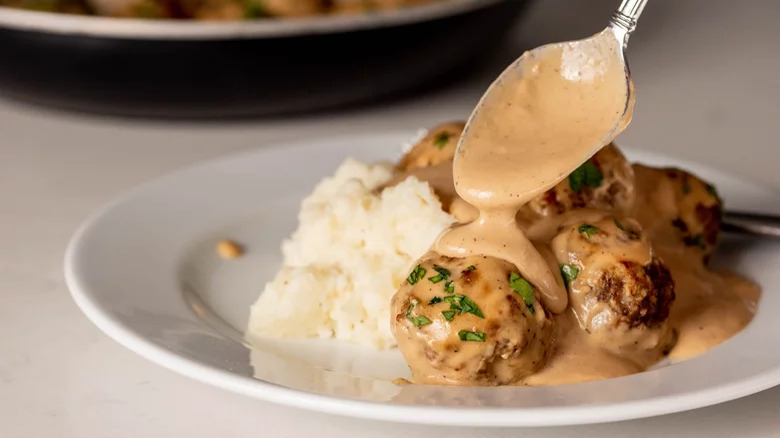 Spooning creamy sauce on meatballs and mash