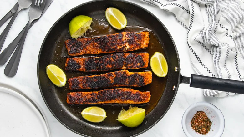 Blackened salmon in a cast iron pan with lime wedges
