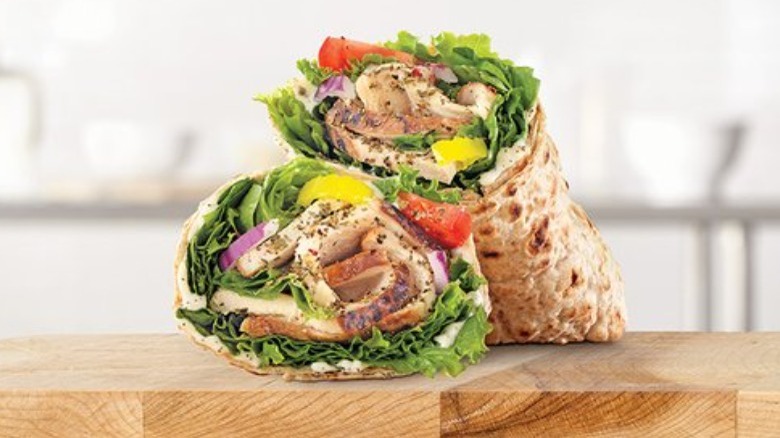 Arby's Creamy Mediterranean Chicken wrap on a wooden cutting board