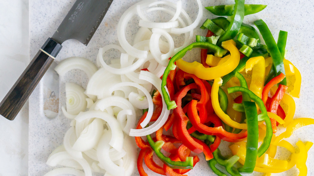 knife next to onions and peppers on cutting board