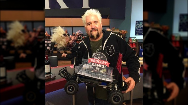 Guy Fieri holding a "Guy's Grocery Games" shopping cart 