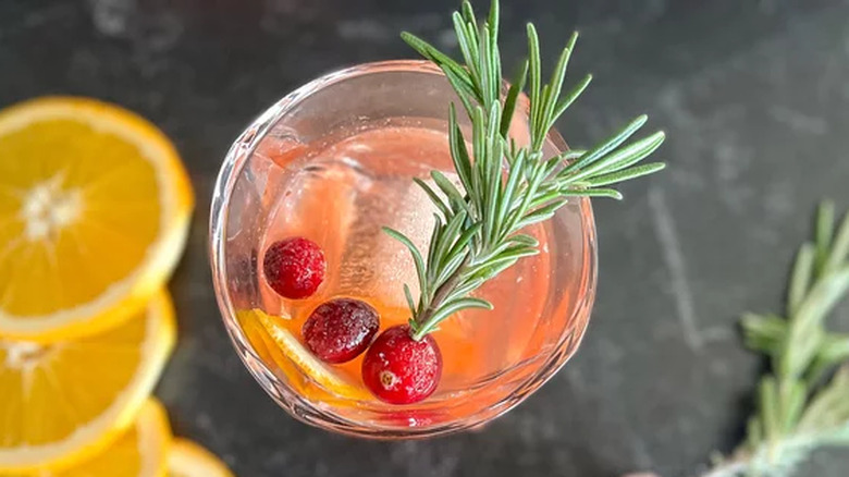 Cocktail with cranberries, rosemary sprigs, and orange slices.