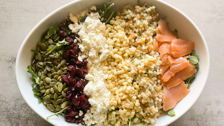 Oval bowl with layers of corn, couscous, salmon, pumpkin seeds. 