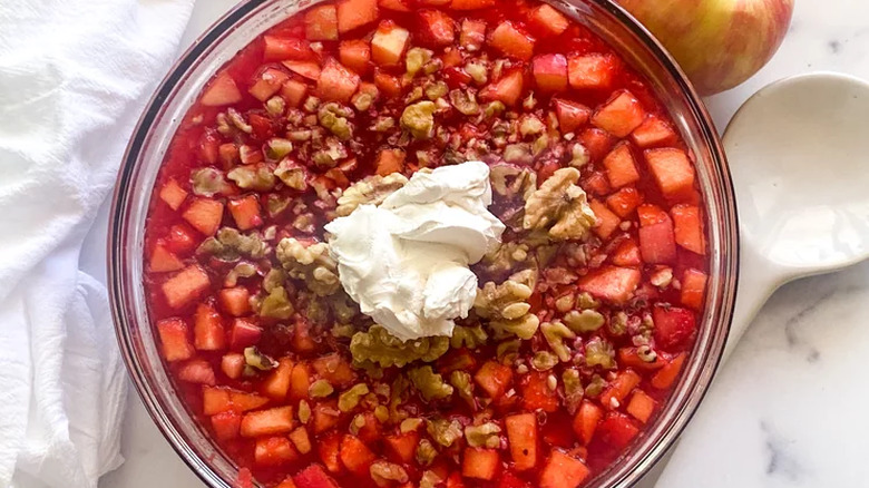 Glass bowl of red gelatin salad with apples and nuts