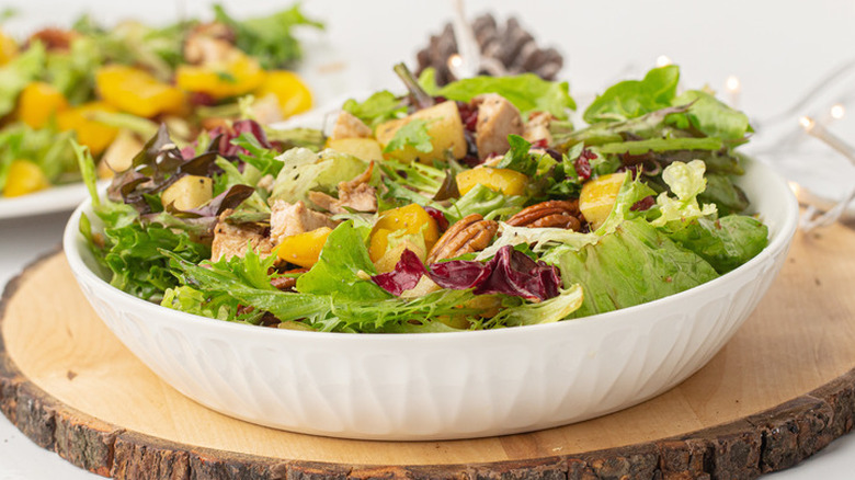 White bowl with pecan, lettuce, and chicken.