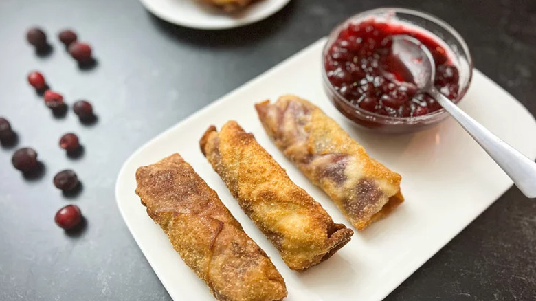 Three egg rolls next to dish of cranberry sauce.