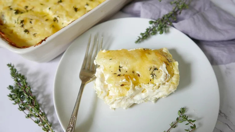 Creamy potatoes in casserole dish and plate with thyme