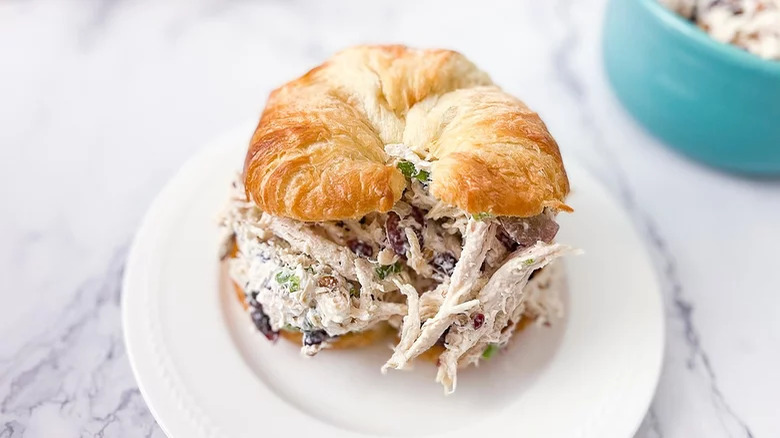 plate with turkey salad with cranberries and pecans on croissant