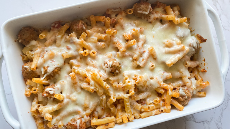 Baked ziti, meatballs, and cheese in a white casserole dish.