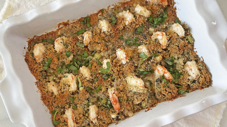 Baking dish with rows of shrimp, herbs, and browned stuffing.