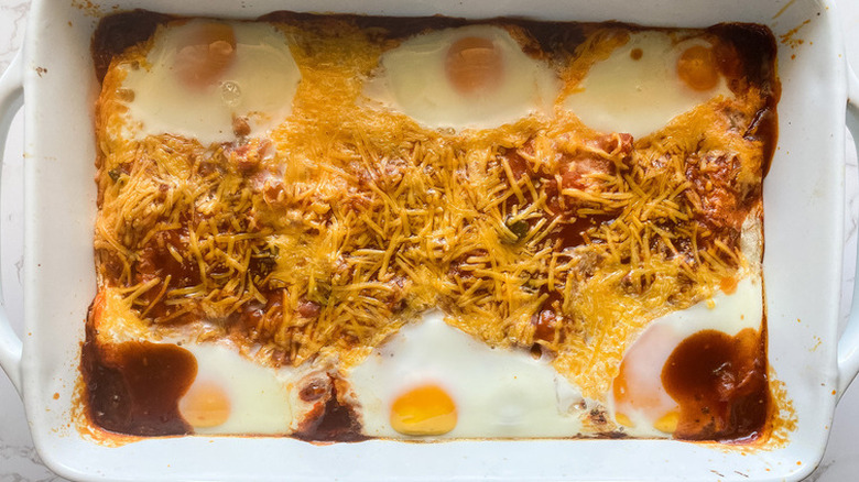 Eggs baked with enchilada sauce and cheese in casserole.