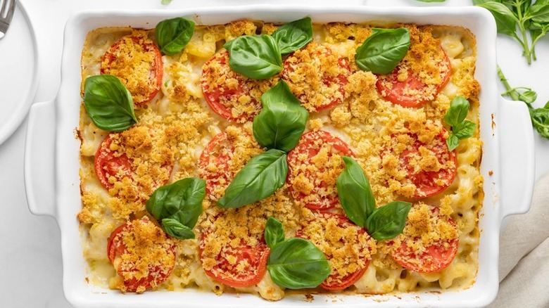 White baking dish with pasta, cheese, tomatoes and basil leaves.