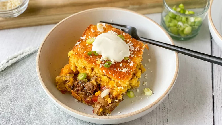 Cornbread-topped casserole slice with ground beef and scallions.