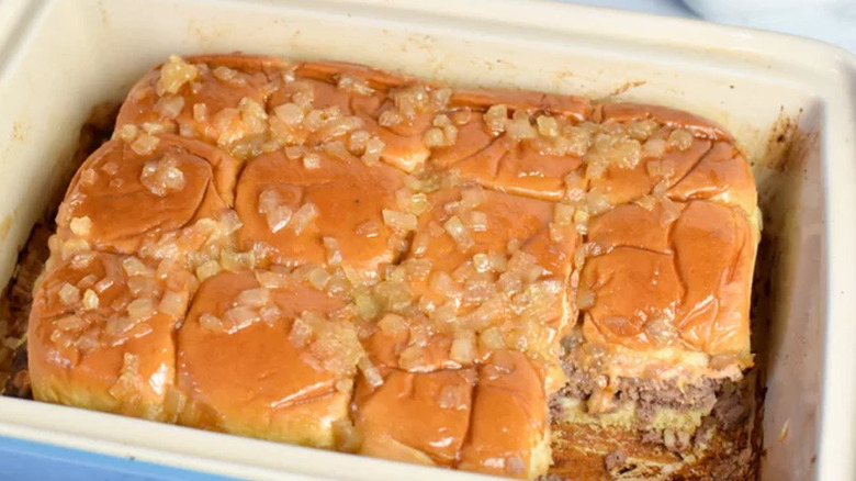 Slider rolls in baking dish with burger and diced onion.