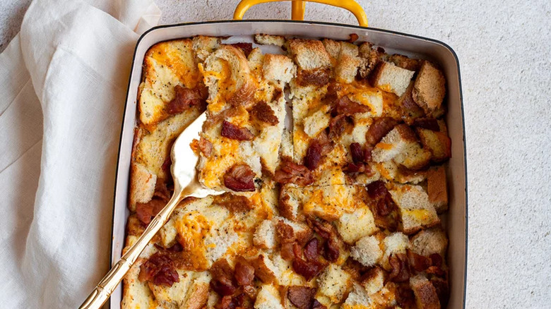 Baked bread, egg, and bacon casserole in rectangular dish.