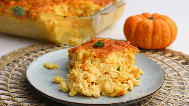 Slice of baked mac and cheese on plate with small pumpkin behind.