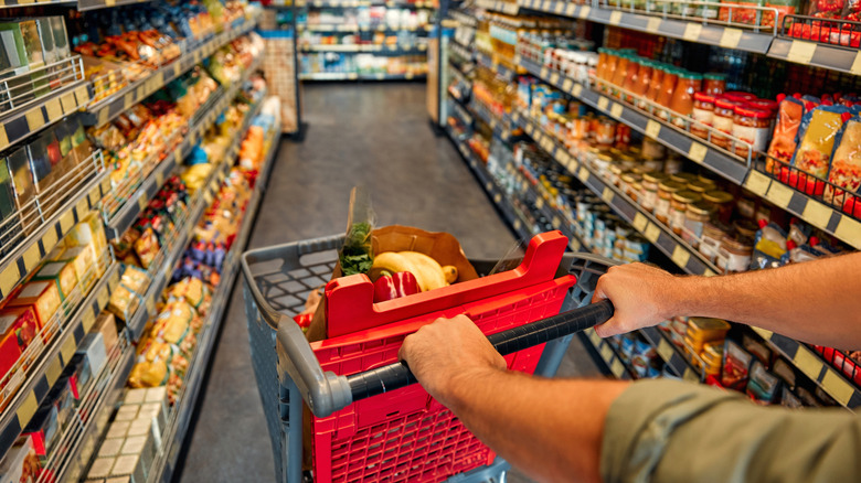 Man pushing red shopping cart through grocery aisle