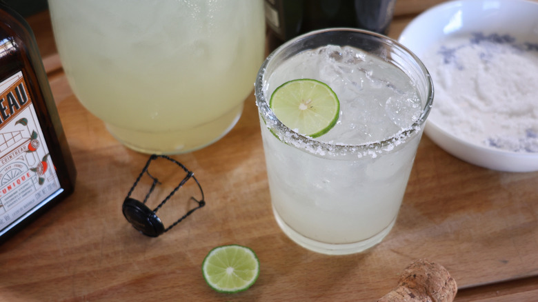 champagne margarita on cutting board with pitchers, bottlles, lime slices, and plate of salt