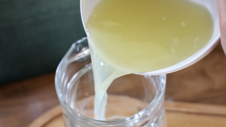 pouring lime juice into glass pitcher from measuring cup