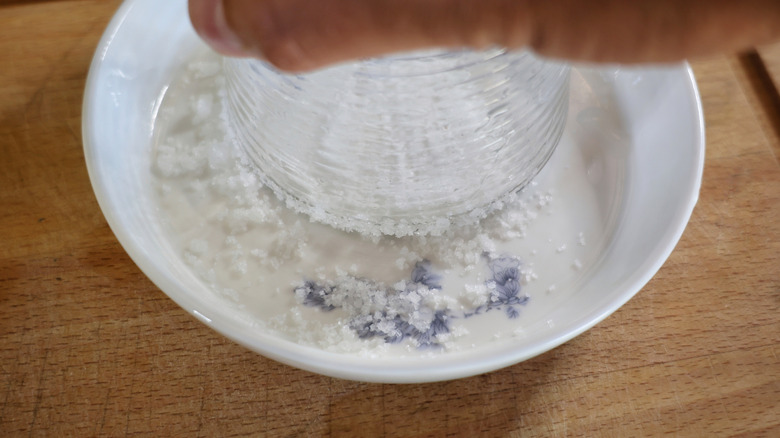 hand holding glass upside down on plate of flaky salt