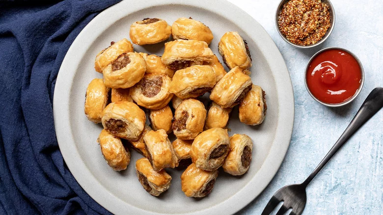 plate of sausage rolls with dipping sauces and fork