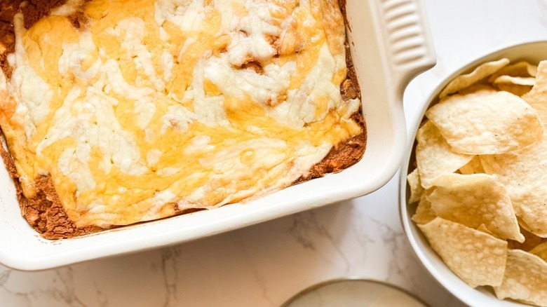 casserole dish of bean dip with bowl of tortilla chips