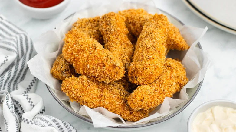 bowl of breaded and baked chicken tenders with dipping sauces on side