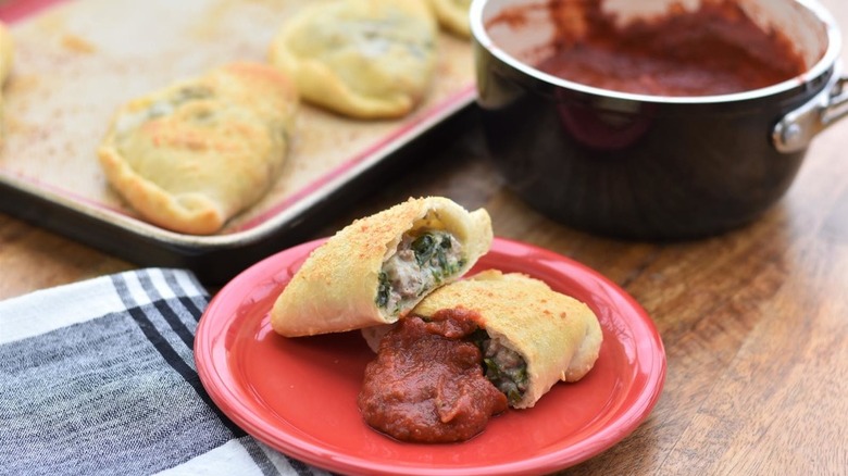 plate and baking sheet of calzones with pot of tomato sauce on side