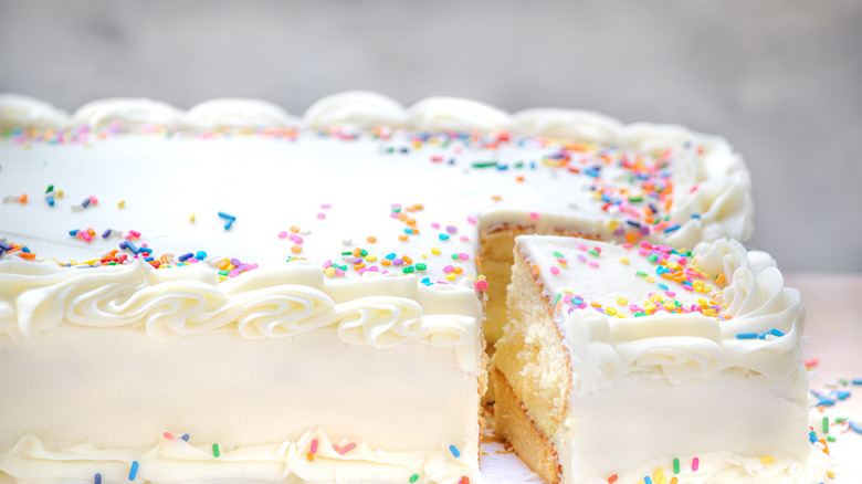 close up of vanilla sheet cake with rainbow sprinkles and slice