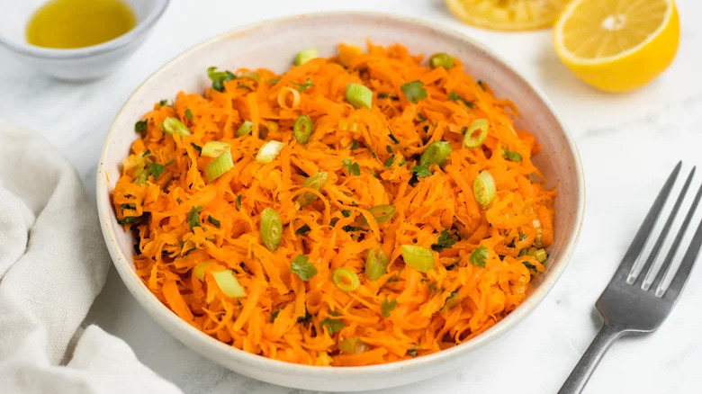 bowl of shredded carrot salad with fork and lemons