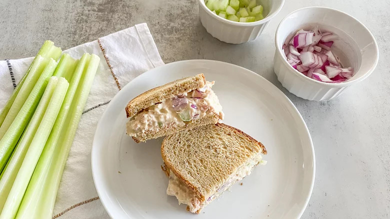 tuna salad sandwich on plate with celery and onions on side