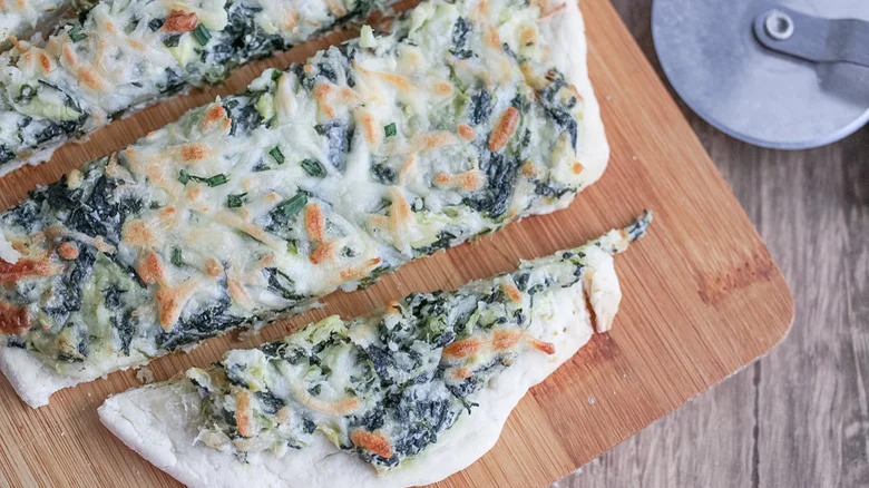 sliced spinach artichoke flatbread on wooden board