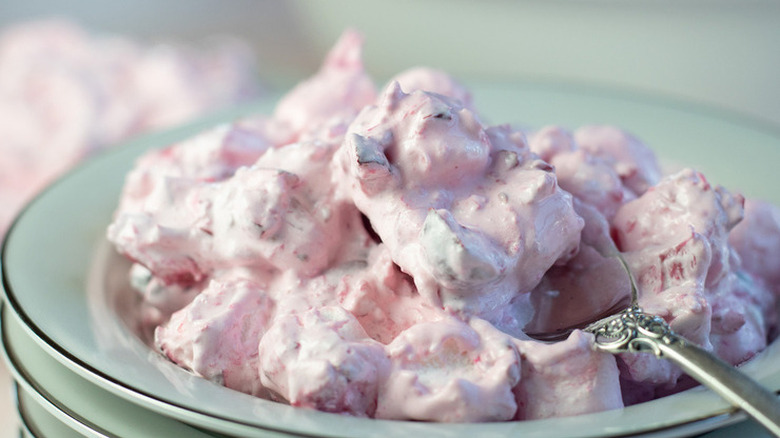 Creamy marshmallow fruit salad in bowl with spoon.