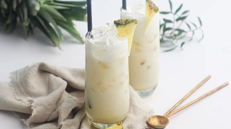 Tall glasses with creamy white coconut drink and pineapple wedges.