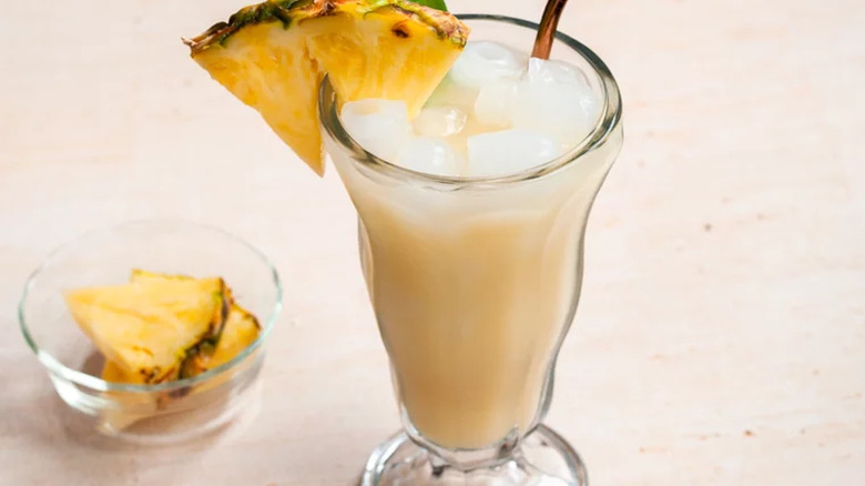 Tall glass with creamy pineapple cocktail and pineapple on rim.