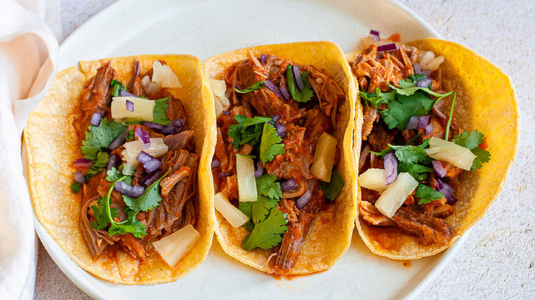 Three taco shells with saucy meat shreds and pineapple.