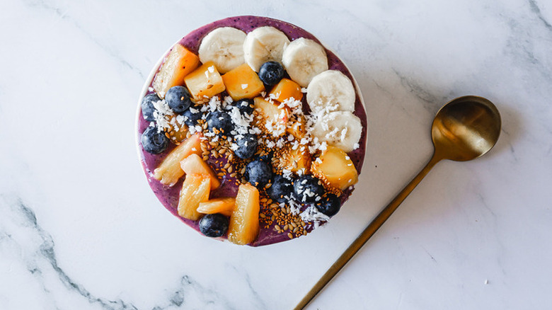 Bowl of blueberry smoothie topped with sliced fresh fruit.