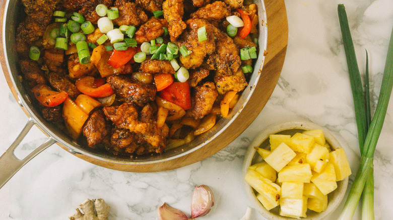 Skillet of stir fried chicken and veggies with dish of pineapple.