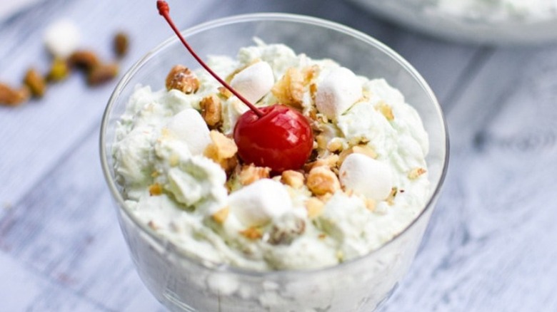 Dish of cream-based salad with nuts and a cherry.