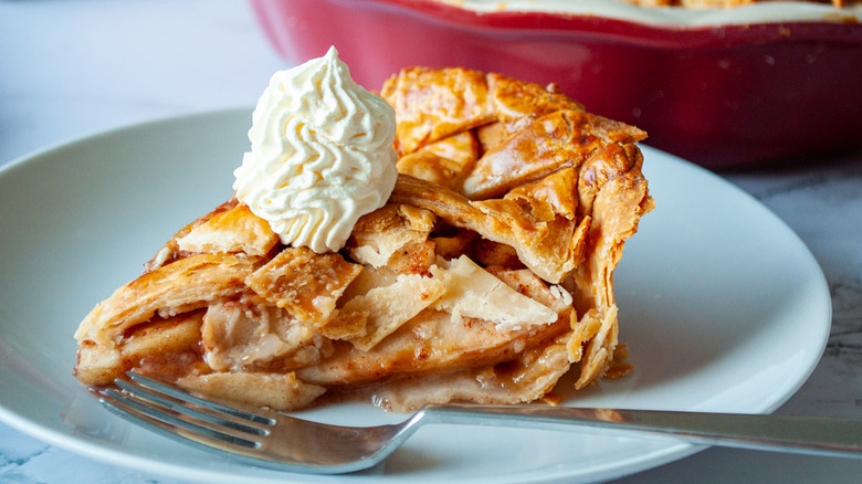 Apple pie slice on plate with fork and whipped cream.