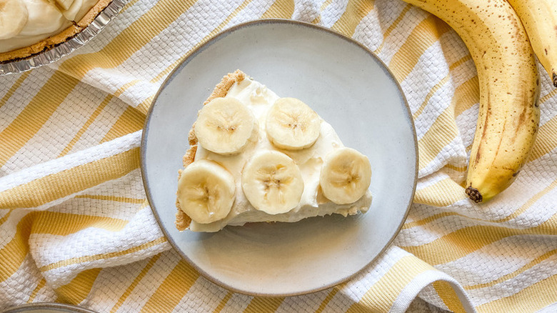 Slice of cream pie topped with sliced bananas on round plate.