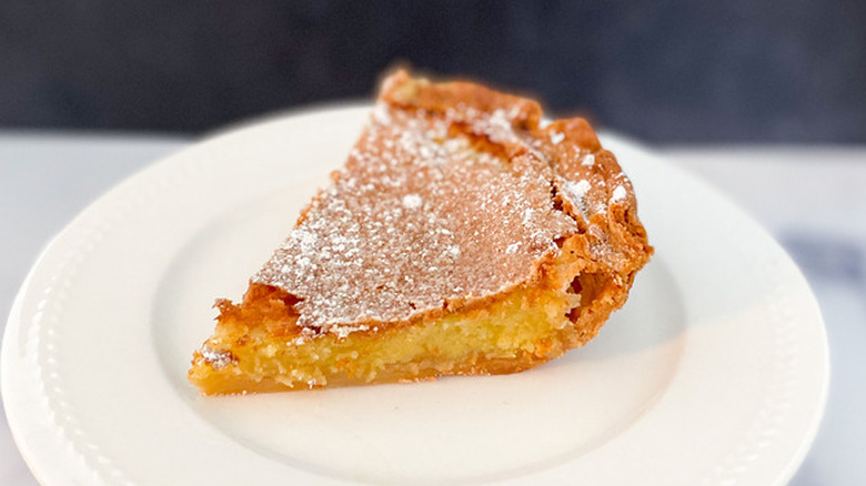 Slice of custardy chess pie with dark top on a white plate. 