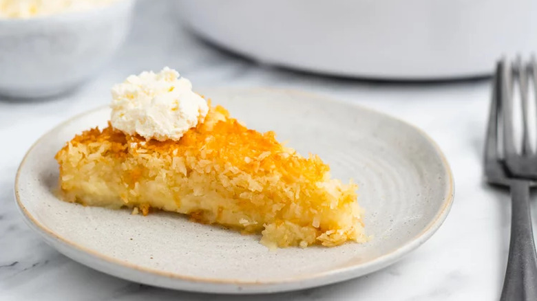 Slice of cream coconut pie with whipped cream on a gray plate.