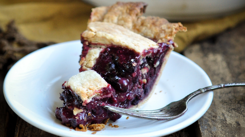 Slice of huckleberry pie with fork on white plate.