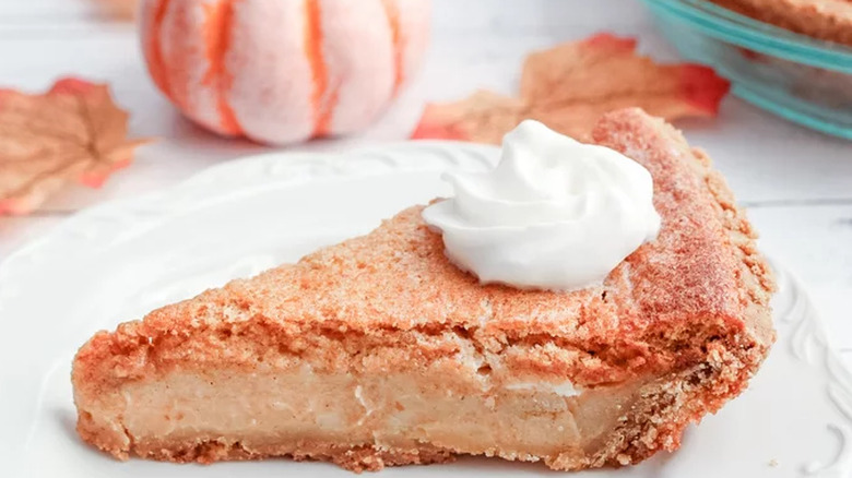 Pumpkin pie slice with whipped cream and fall decor on table.