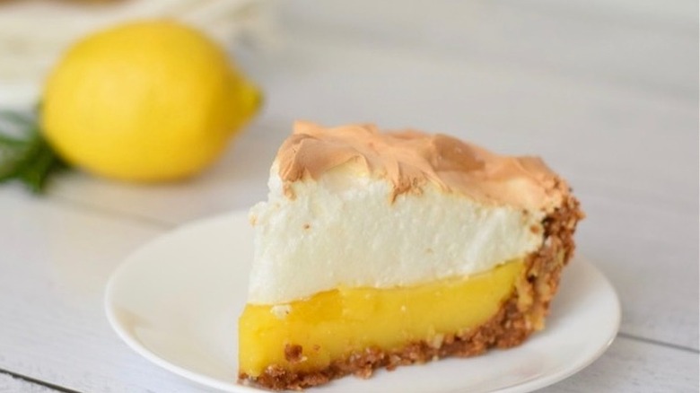 Slice of meringue-topped lemon pie on white plate.