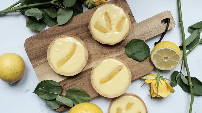 Four small lemon tarts with lemons and lemon leaves.