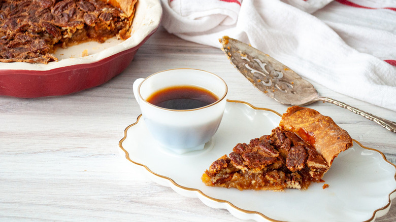 Pecan pie slice with coffee on white plate.