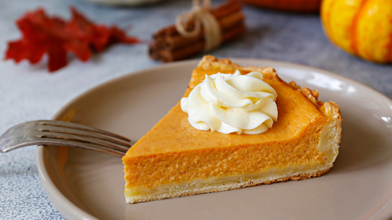 Slice of pumpkin pie on tan plate with fork. 