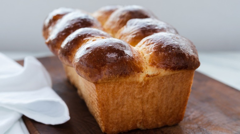 loaf of brioche bread on wooden cutting board with dish towel